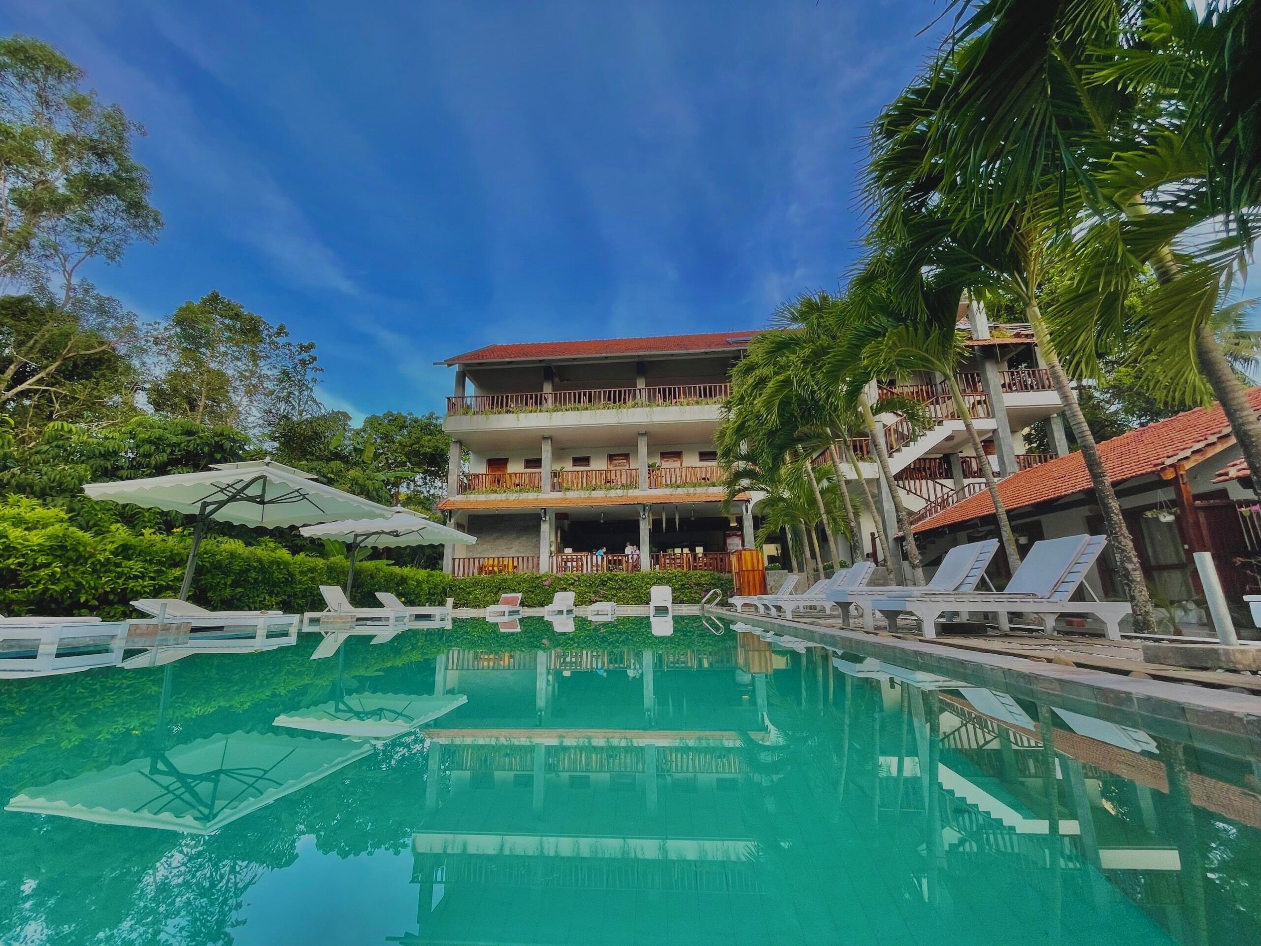 A hotel with a pool, multiple balconies, and lush greenery.