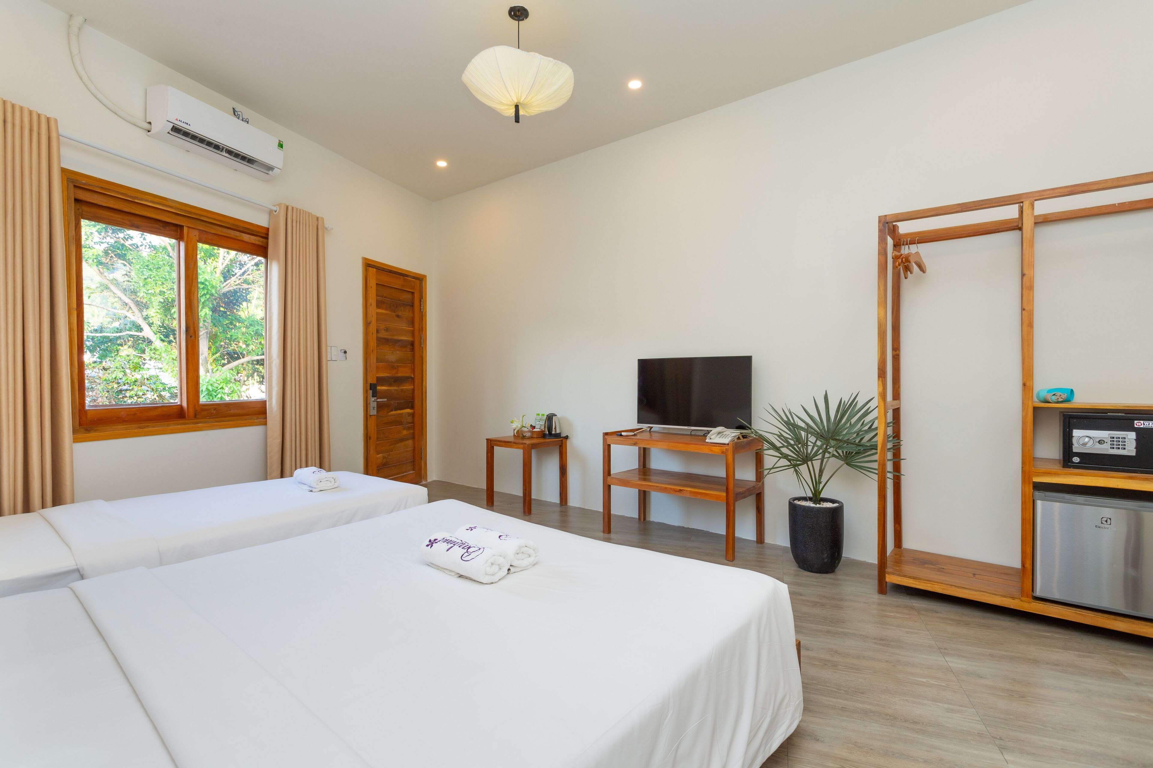 A hotel room with two beds, a TV, a small table, a potted plant, and a minibar.