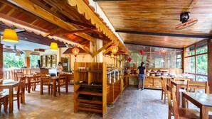 Un restaurante con mobiliario de madera, una barra central de servicio y amplios ventanales que permiten la entrada de luz natural.