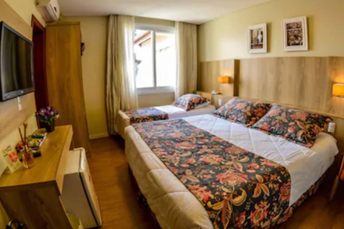Hotellihuone, jossa on kaksi sänkyä, työpöytä, televisio ja ikkuna, jossa on verhot.