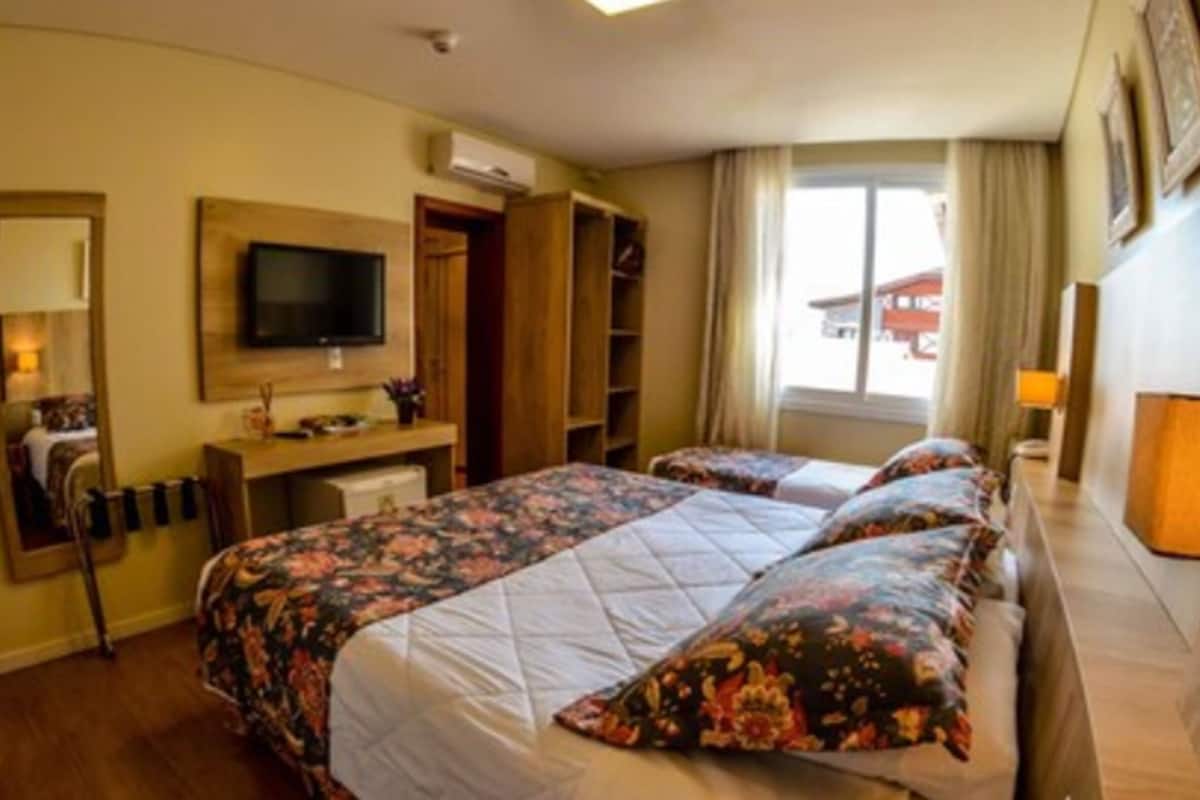 Hotellihuone, jossa on kaksi sänkyä, televisio, työpöytä ja ikkuna, jossa on verhot.