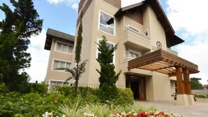 A multi-story residential building with a covered entrance and a landscaped garden with red and white flowers. - Pousada Aconchego da Borges (Gramado)