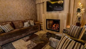 A living room with a sofa, armchairs, a fireplace, and a TV mounted above it. - Pousada Aconchego da Borges (Gramado)