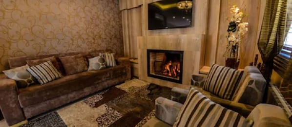 A living room with a sofa, armchairs, a fireplace, and a TV mounted above it. - Pousada Aconchego da Borges (Gramado)