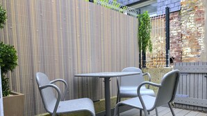 Terrassa a l'aire lliure amb taula i quatre cadires, tanca de bambú i mur de maó.