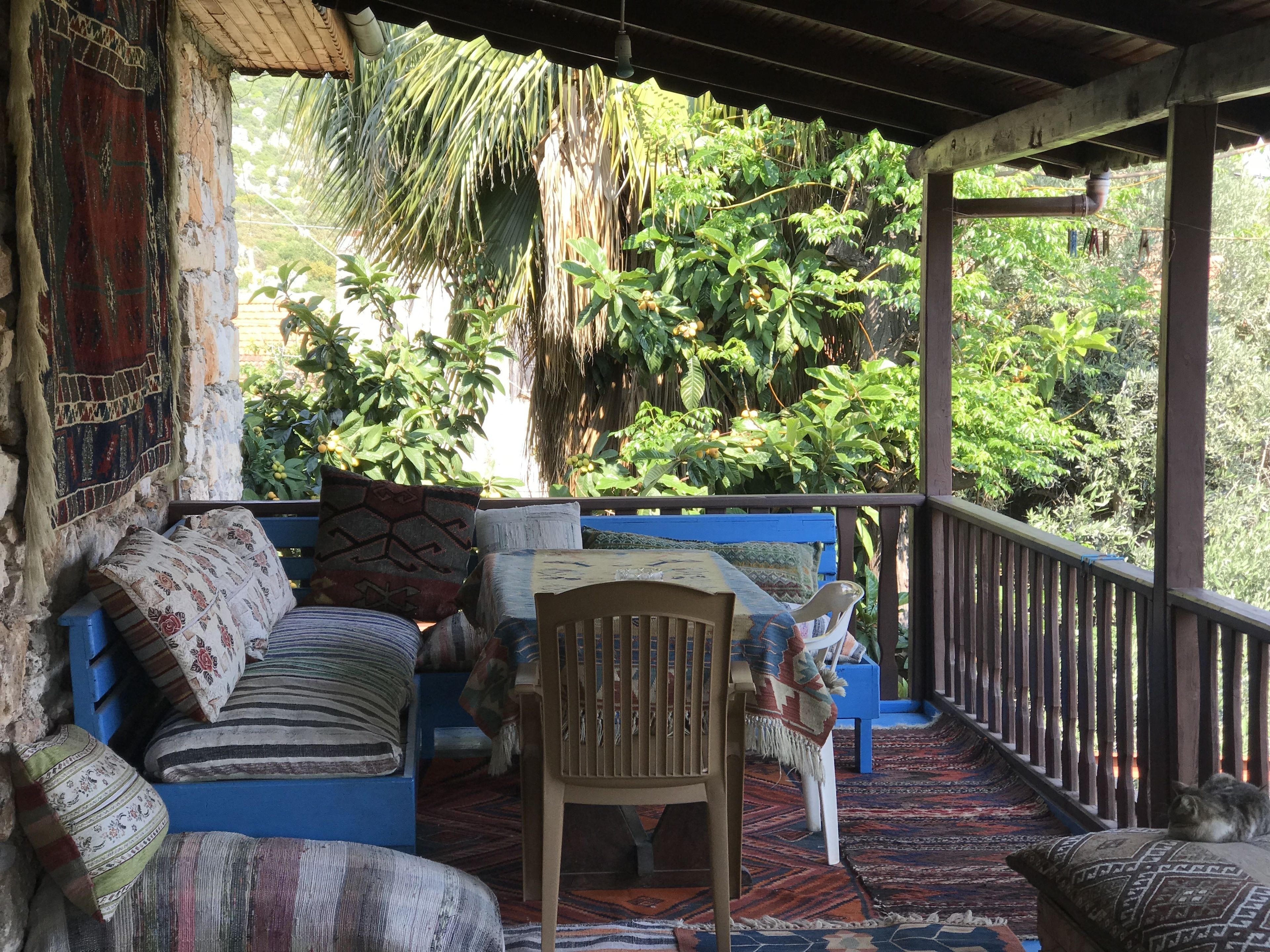A covered porch with a blue sofa, patterned cushions, and a wooden chair.
