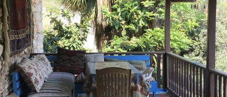 A covered porch with a blue sofa, patterned cushions, and a wooden chair.