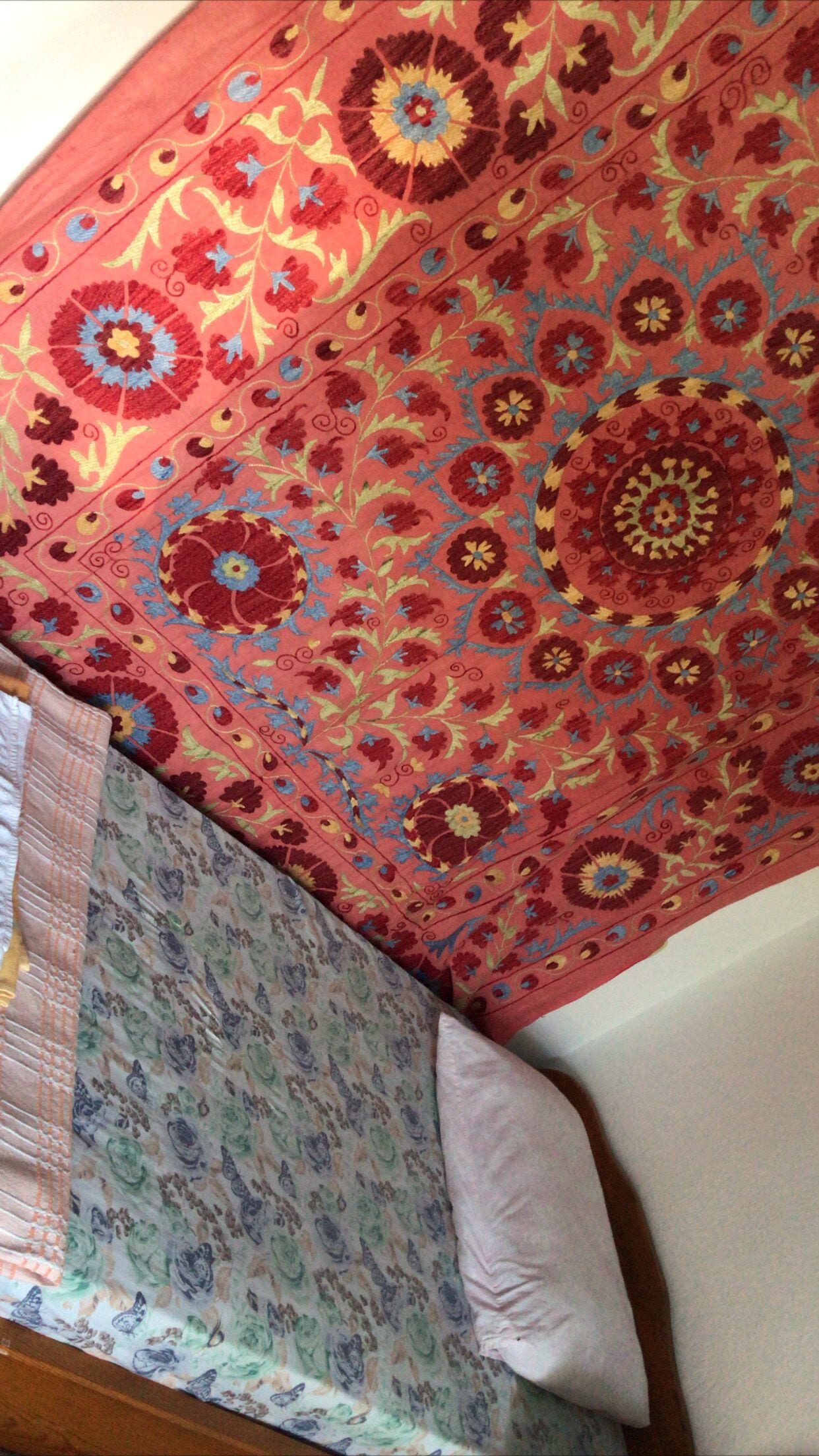 Una cama con colcha estampada de flores y una almohada lisa.
