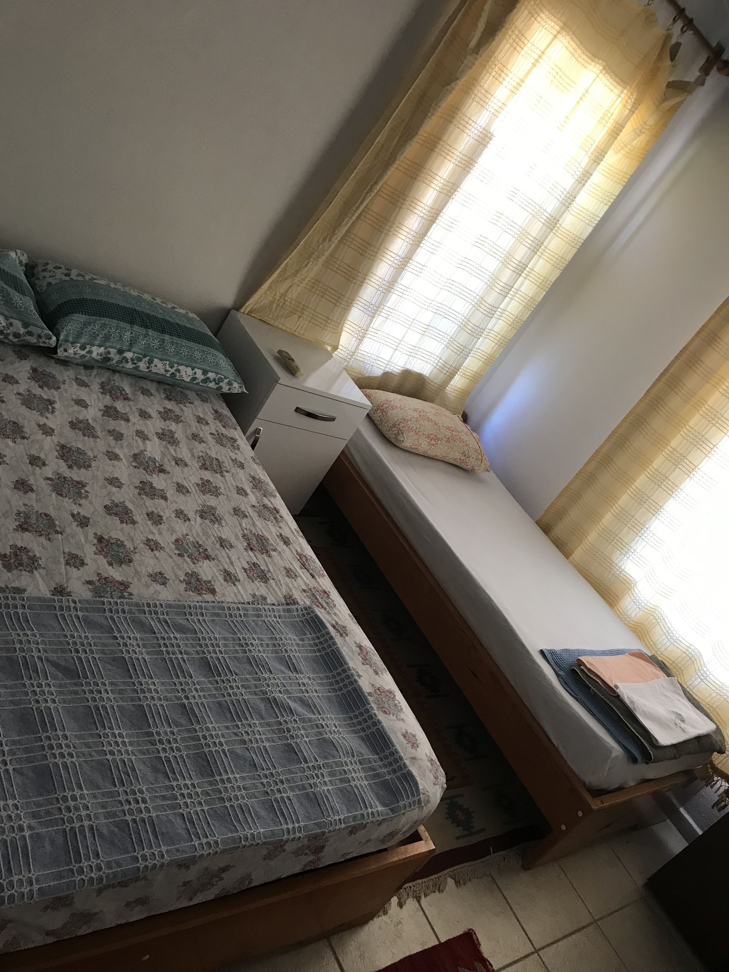 A bedroom with a bed, a small bedside table, and a window with curtains.