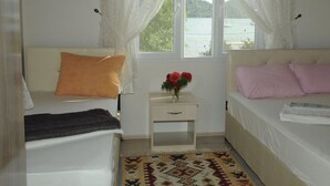 Ein Schlafzimmer mit zwei Betten, einem Nachttisch mit Blumenvase und Blick auf ein Gewässer durch transparente Vorhänge.