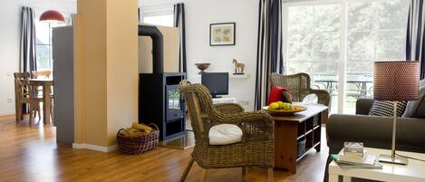 A modern living room with a sofa, wicker chairs, a dining table, and a television.
