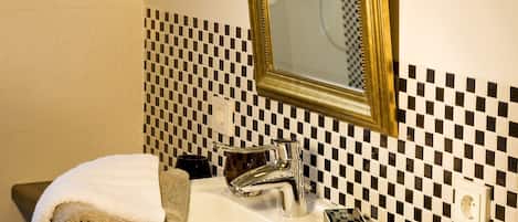 Un bagno con zoccolo a scacchi, un lavandino bianco con specchio dorato e asciugamani sul piano di lavoro.