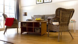 A living room with wicker chairs, a sofa, a wooden coffee table with fruits, and a lamp.
