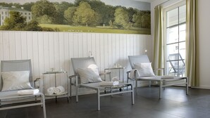 A room with three lounge chairs, a small table, and a mural of a landscape.