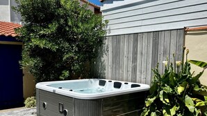 Un jacuzzi dans un jardin, avec une terrasse en bois, un pot de fleurs et une clôture.