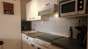 Een kleine keuken met witte kasten, een ingebouwde magnetron, een vaatwasser en een fornuis.