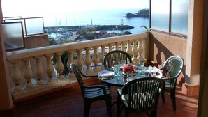 Een balkon met een eettafel, met uitzicht op een kustgebied met gebouwen en een jachthaven.