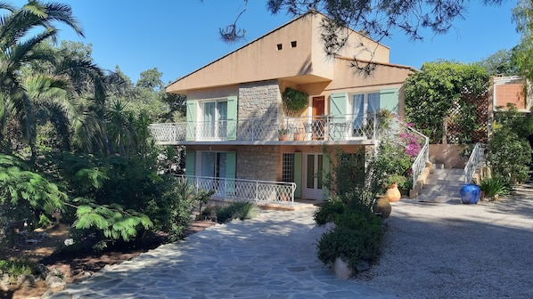 A two-story house with a stone facade, a balcony with a white railing, and a gravel driveway.