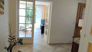 A spacious hallway with tiled flooring leading to a glass door opening to a balcony. A potted plant is visible on the left.