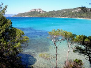 A coastal landscape with clear turquoise waters, a sandy beach, and a mountainous backdrop.