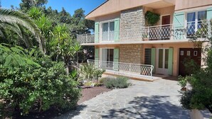 A two-story building with a stone facade, green shutters, and a balcony with a white railing.