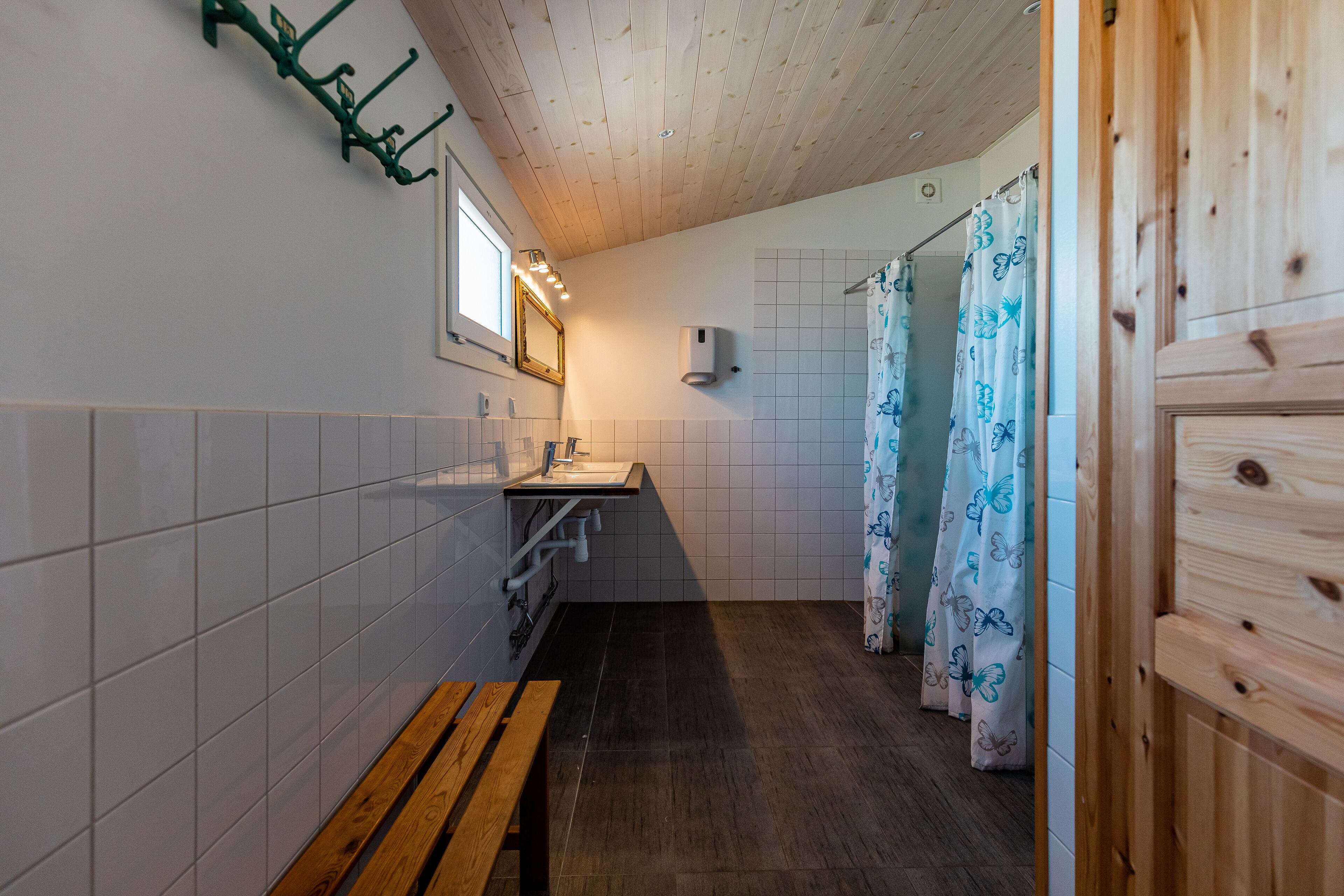 Une salle de bain avec un banc en bois, un lavabo, un miroir et un rideau de douche orné de motifs de papillons.