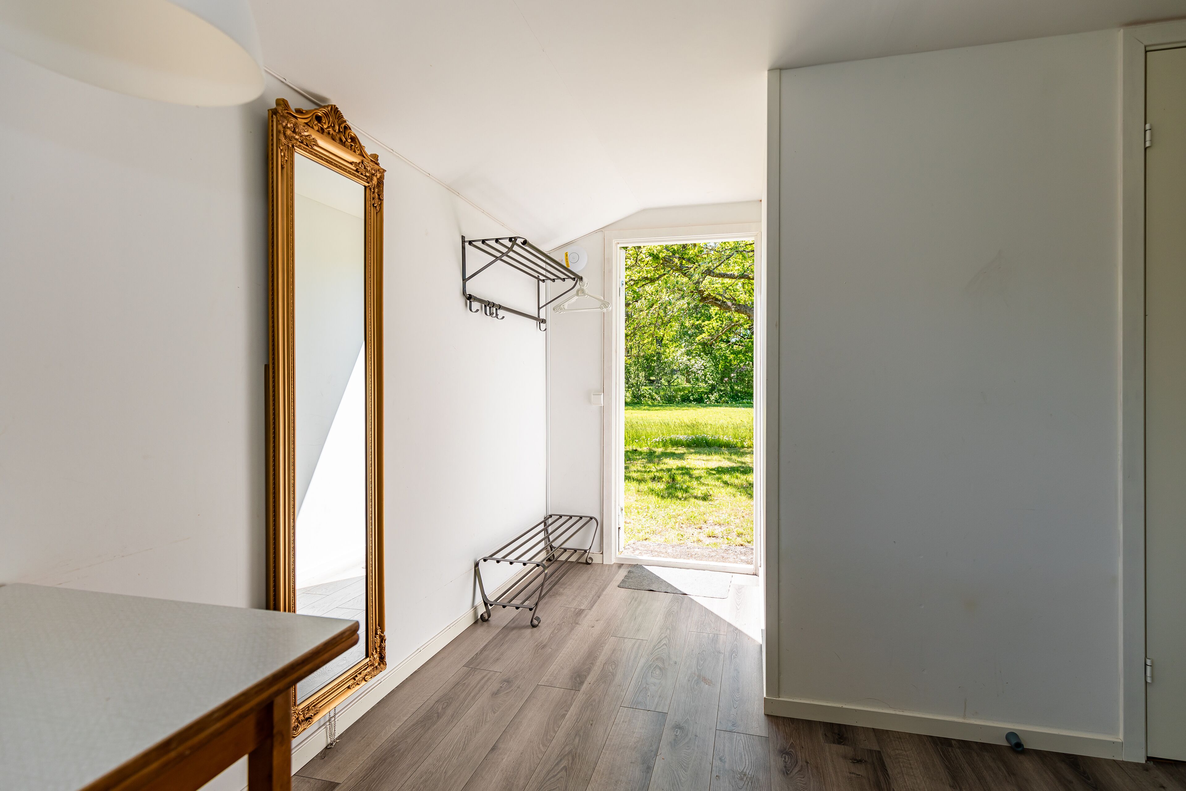 A room with a large mirror, a metal drying rack, and a view of a green outdoor area.