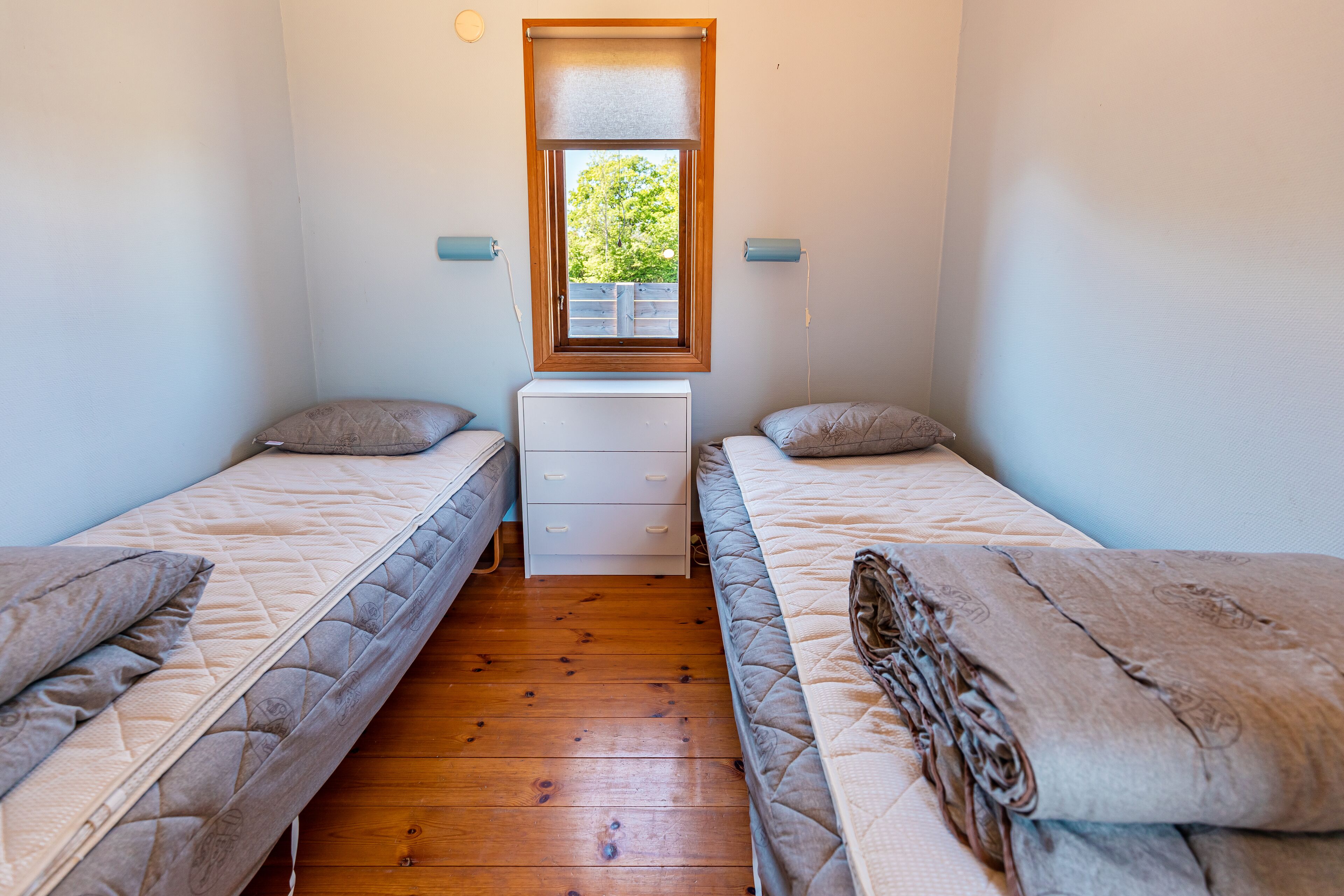 A small room with two beds, a window, and a white dresser.