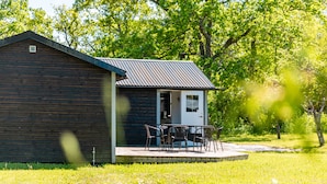 A small wooden cabin with a metal roof, a porch with chairs, and a door leading inside. - Fårösunds Semesterby (Fårösund)