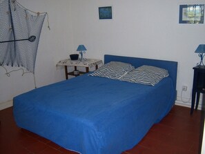 Une chambre avec un lit simple, une petite table avec une lampe et une étagère fixée au mur.