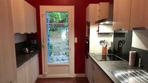 Una cocina funcional con una pared roja, un ventanal de vidrio que da a un jardín y electrodomésticos modernos.