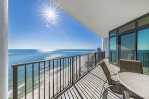 A balcony with a view of the ocean, a table, and chairs.