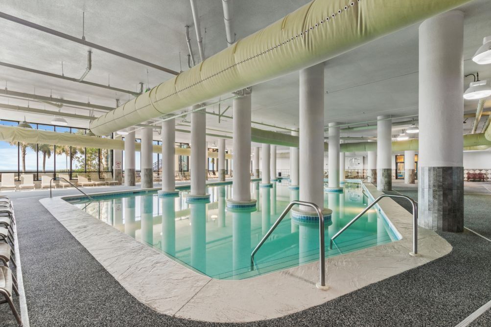 An indoor swimming pool with clear water, surrounded by white pillars, and a tiled floor.