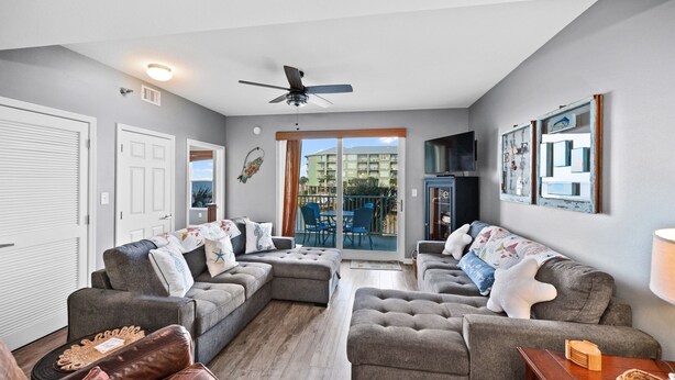 A living room with grey sofas, a ceiling fan, and a large window overlooking a balcony.