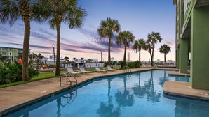 A swimming pool with lounge chairs, palm trees, and a view of buildings in the background.