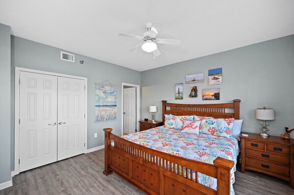 A bedroom with a wooden bed, two bedside tables, a ceiling fan, and a door with a vent.