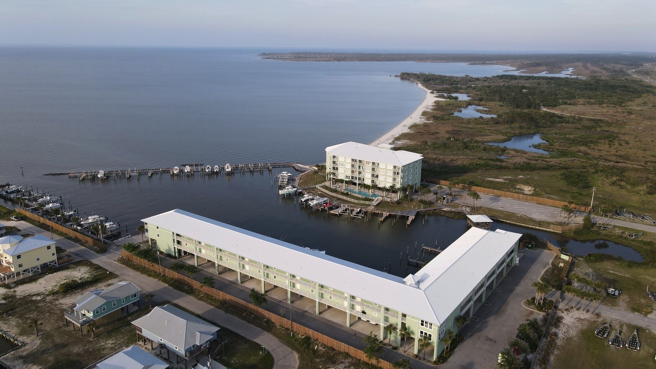 Luftaufnahme eines Küstenhotels mit einem großen Gebäude, einem Hafen mit Booten und einem Strand im Hintergrund.