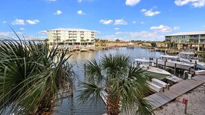 A marina with boats docked, a large building with multiple floors, and a clear blue sky with scattered clouds.