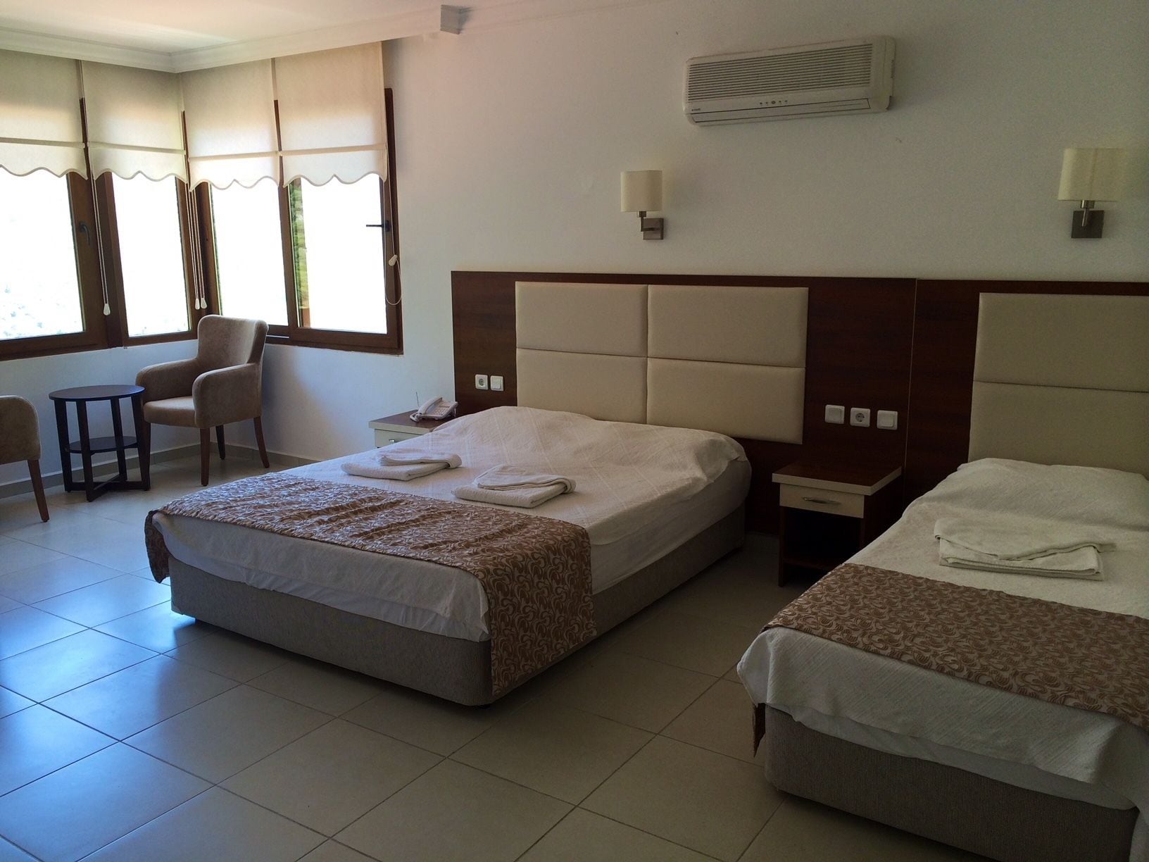 Habitación de hotel con dos camas, una silla, una mesita y una ventana con cortinas.