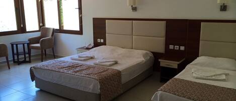 A hotel room with two beds, a chair, a small table, and a window with curtains.