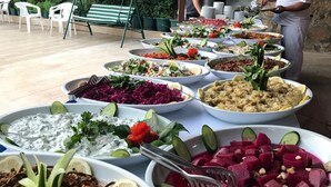 An outdoor buffet with various dishes, a chef preparing food, and a stone wall in the background.