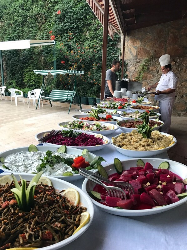 An outdoor buffet with various dishes, a chef preparing food, and a stone wall in the background. - Aygul Hotel (Fethiye)