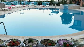 Zona de piscina con sillones de descanso y una mesa de buffet con distintos platos.