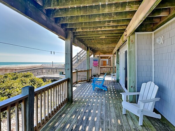 Relax on the deck with a view of the beach, featuring two Adirondack chairs and a flag.