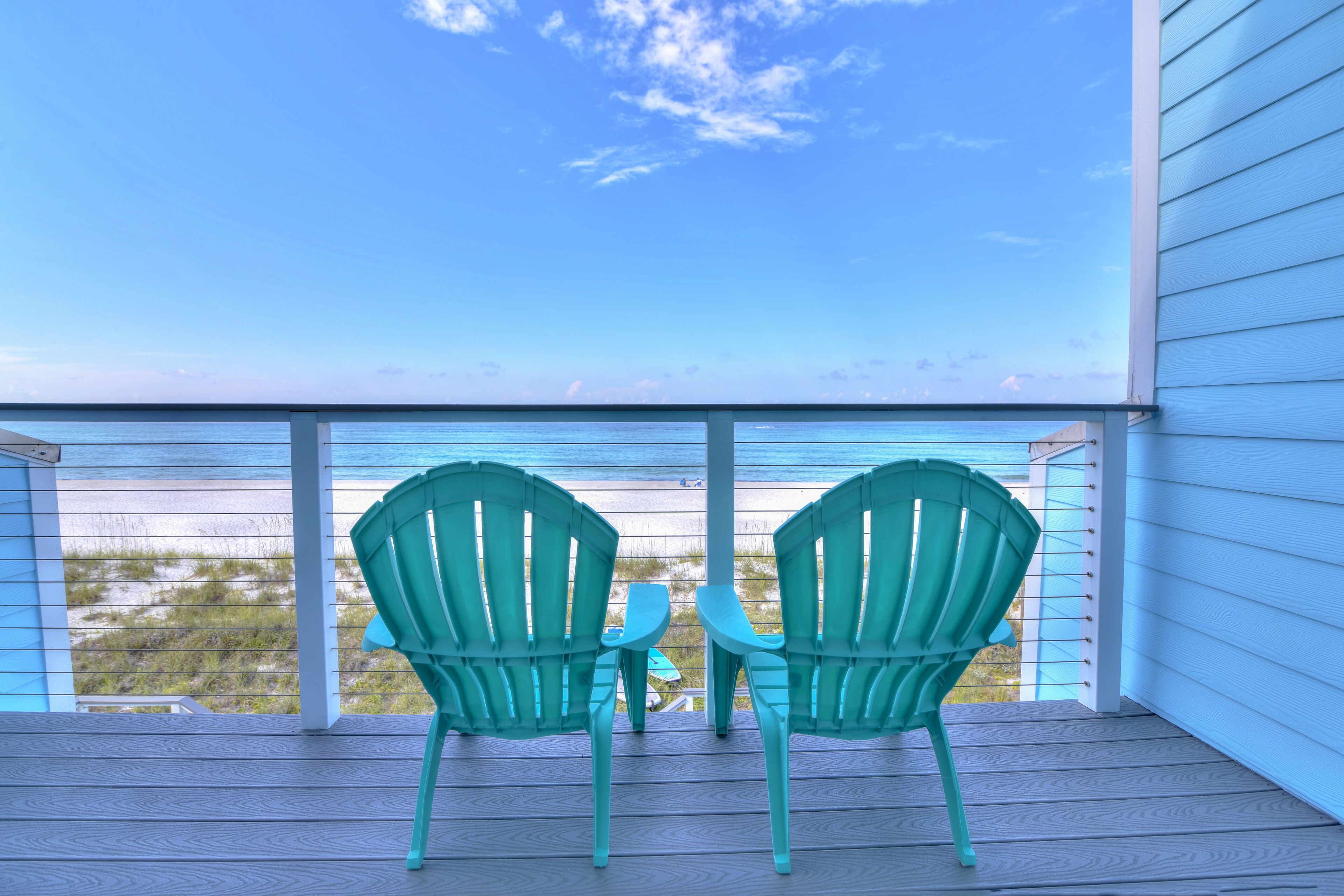 Un balcon avec deux fauteuils Adirondack verts et une petite table, donnant sur une plage et l’océan.