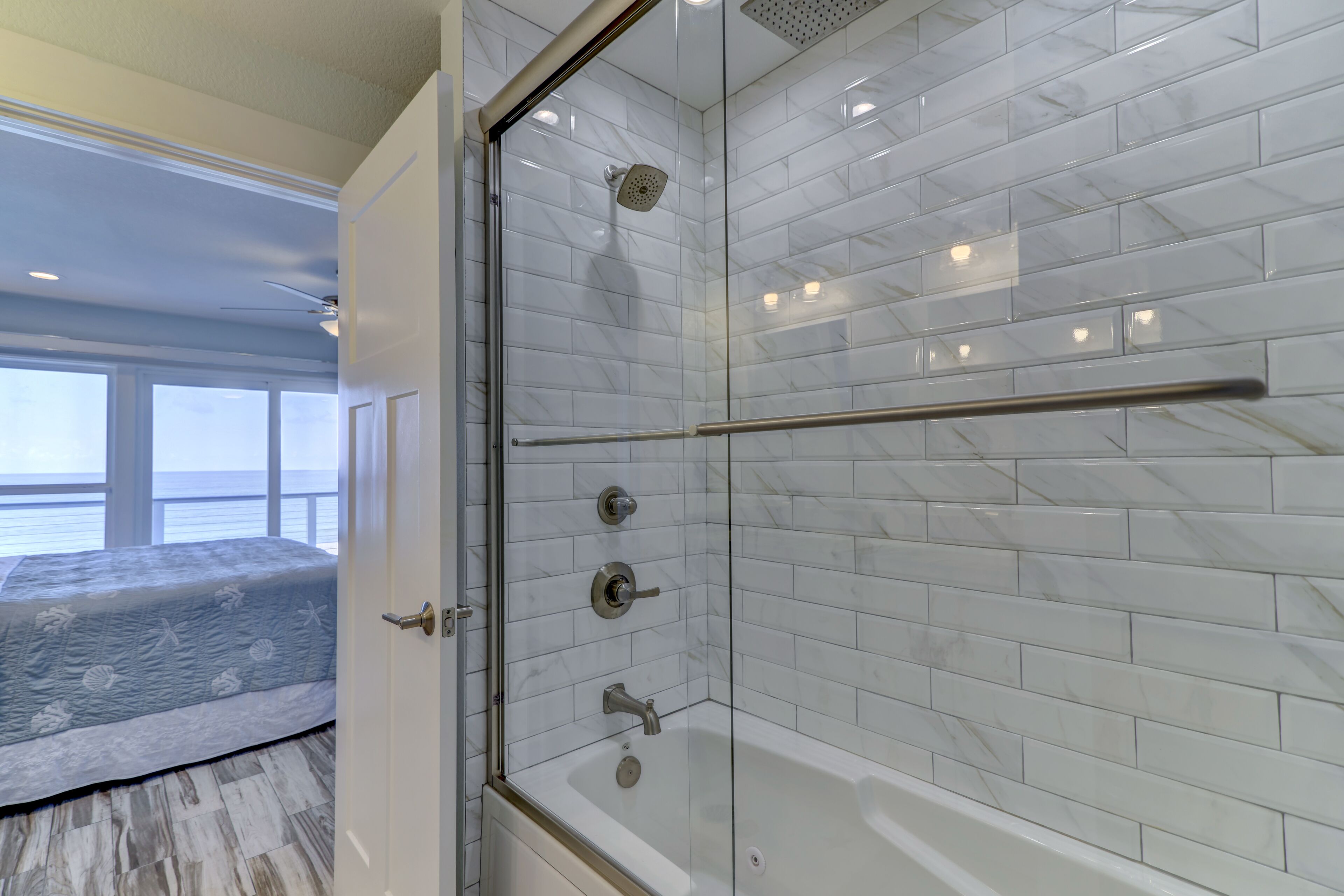 Ein modernes Badezimmer mit einer Duschkabine, weißen Marmorfliesen und einer sichtbaren Badewanne.