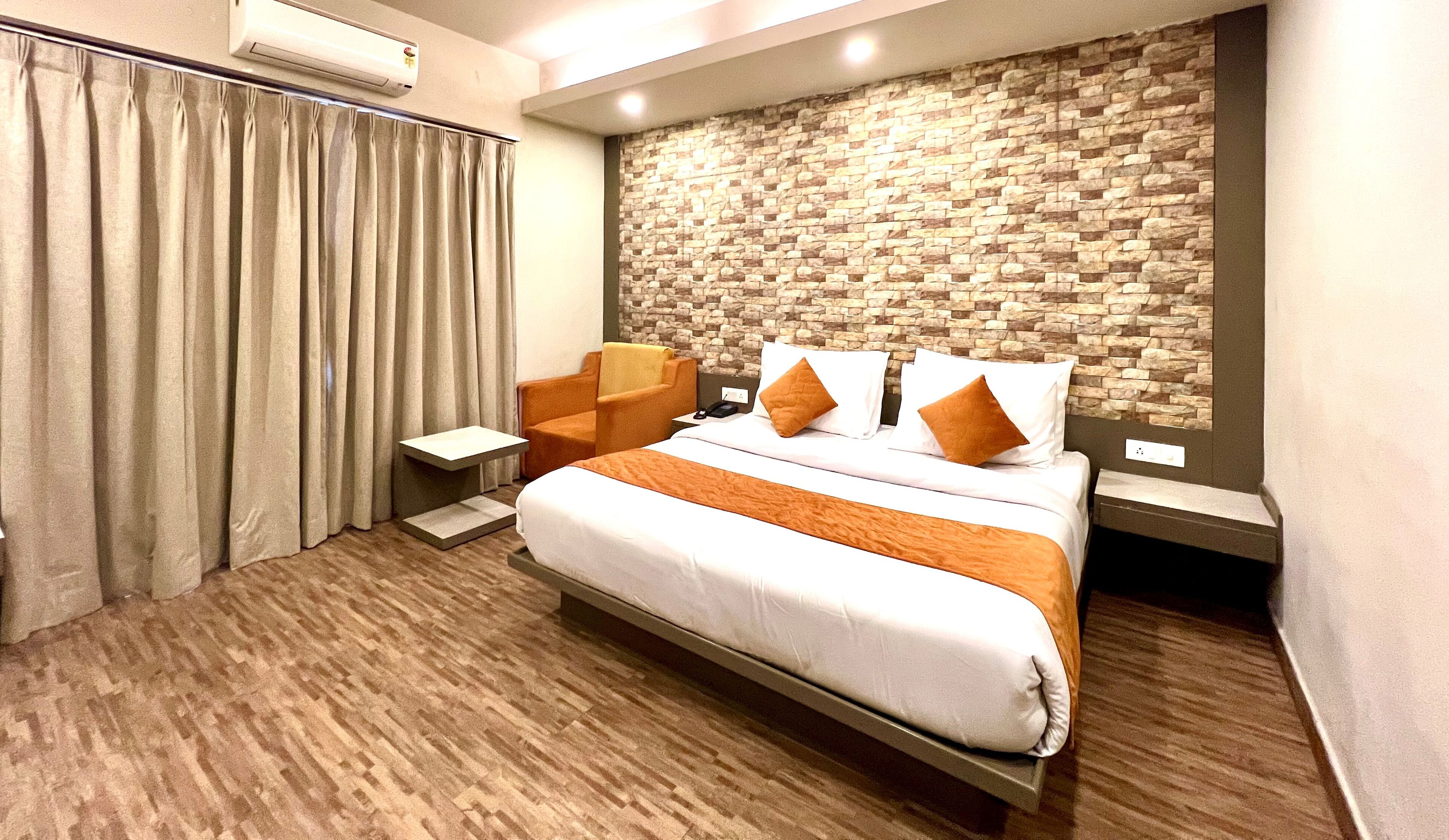 A modern hotel room with a large bed, a seating area, and a stone-patterned wall.