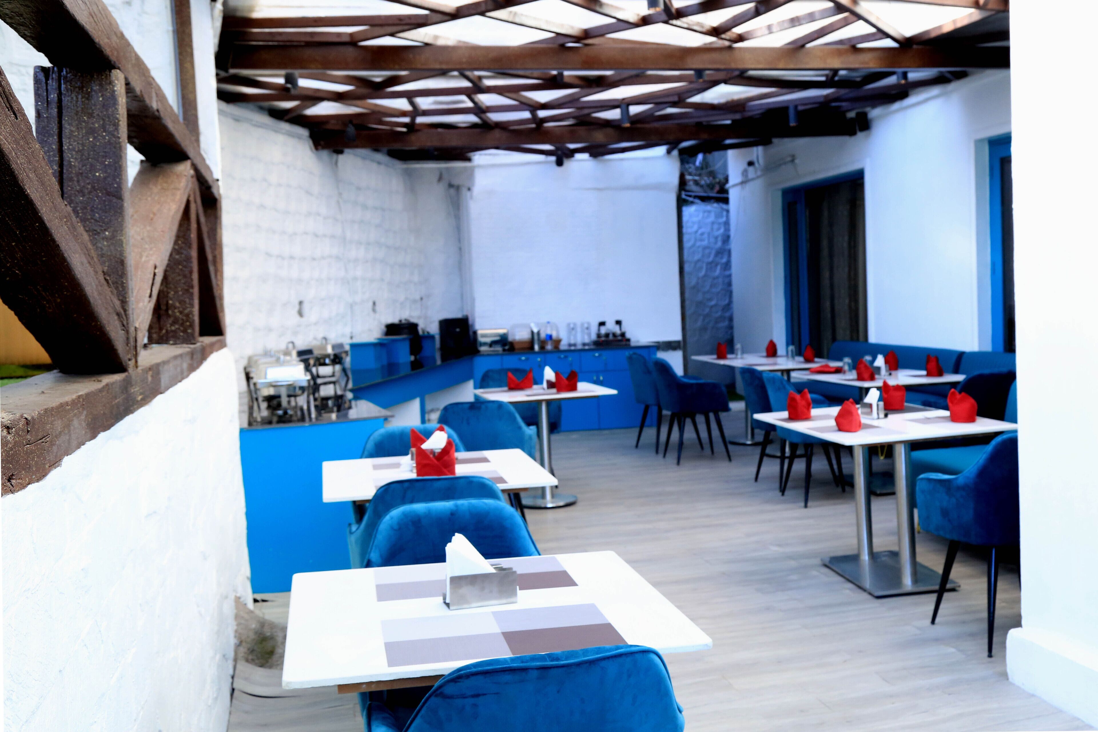A restaurant with blue chairs and white tables, a brick wall, and a wooden ceiling.