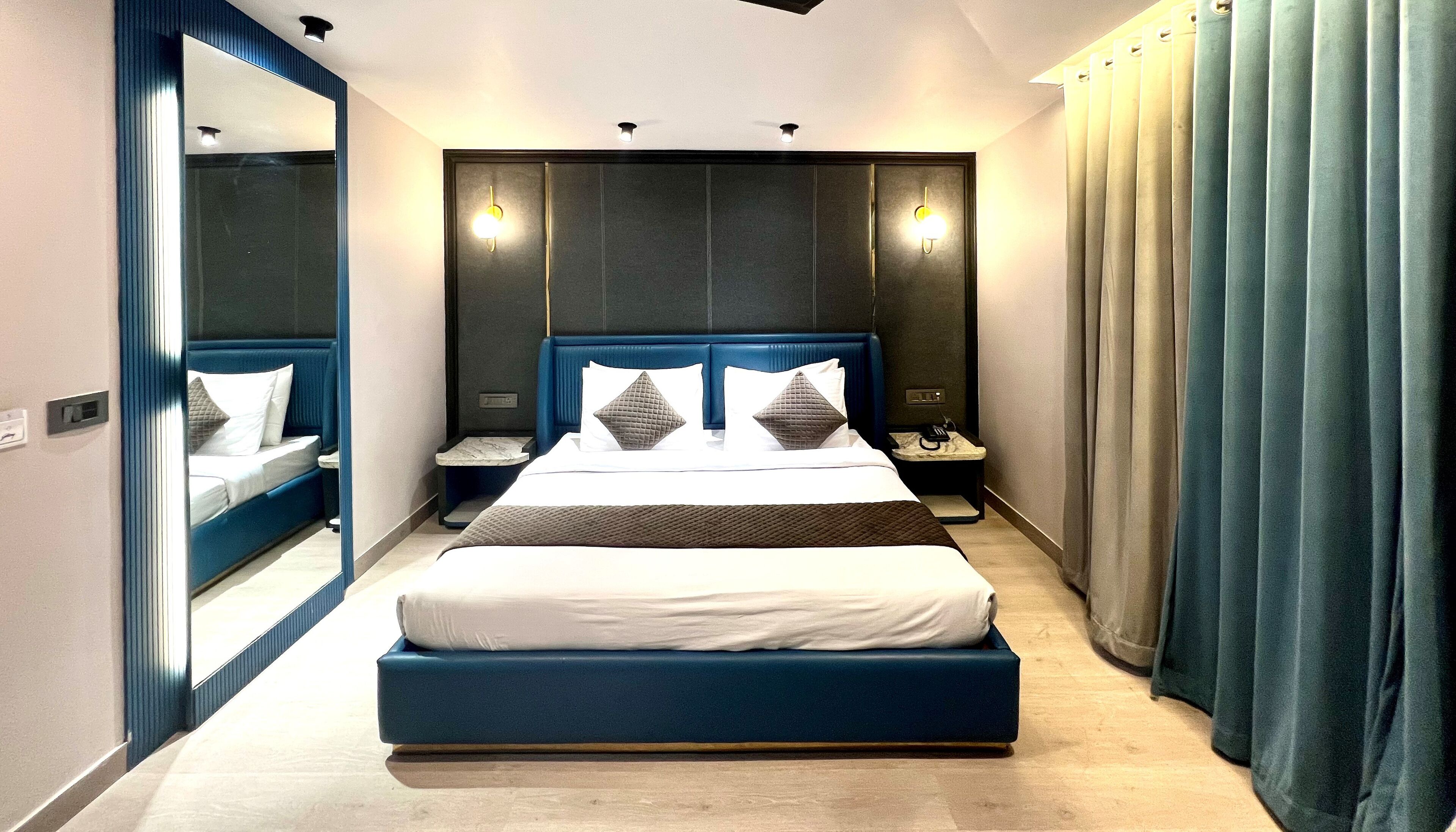 Una habitación de hotel moderna con una cama grande, una mesita de noche, un espejo y una ventana con cortinas.