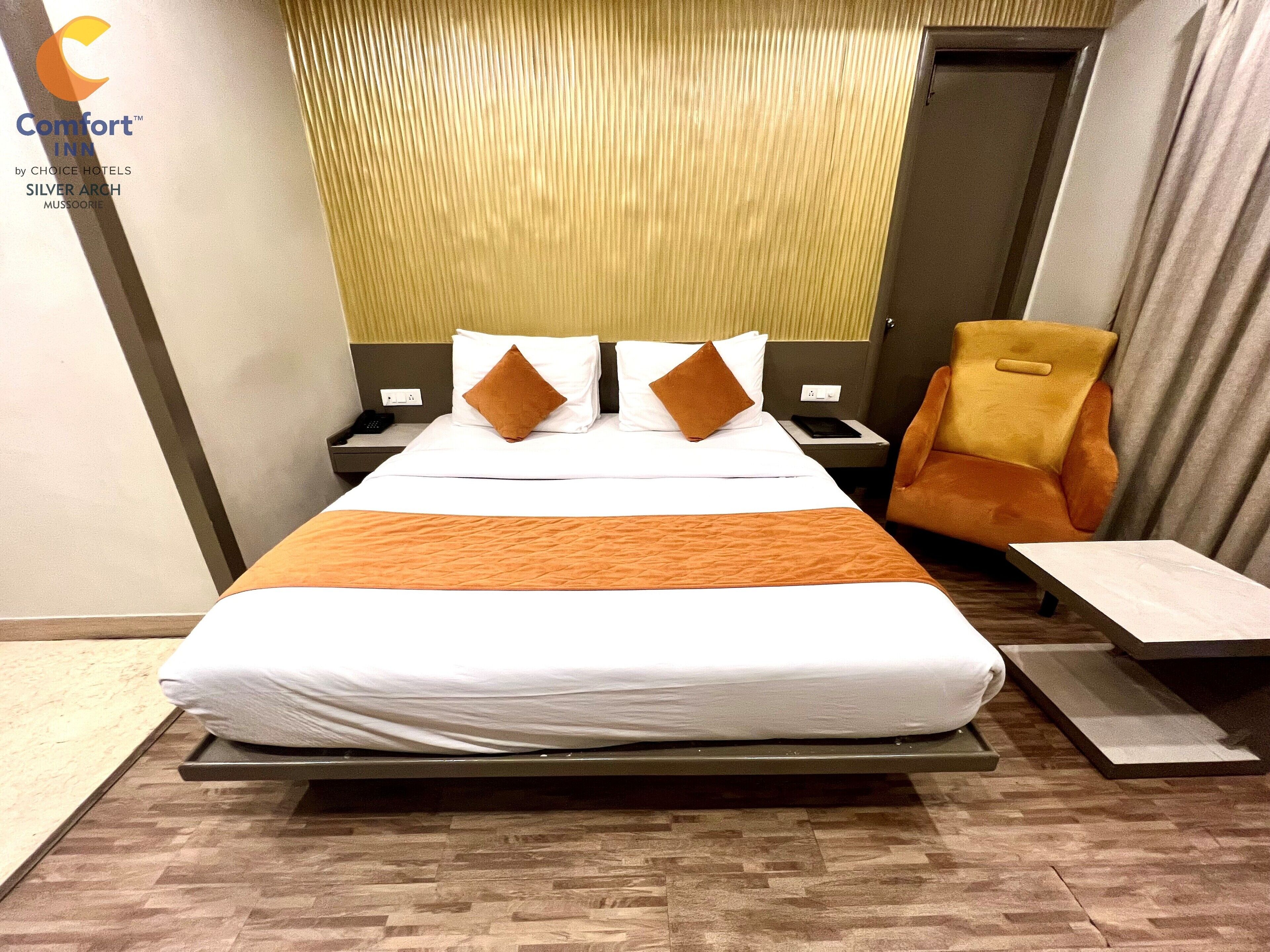 A hotel room with a bed, a chair, a bedside table, and a wall-mounted phone.